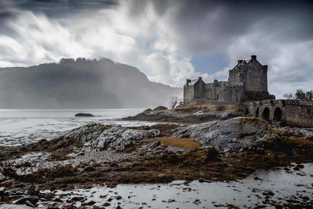 a castle on a rocky beach with Eilean Donan in the background
