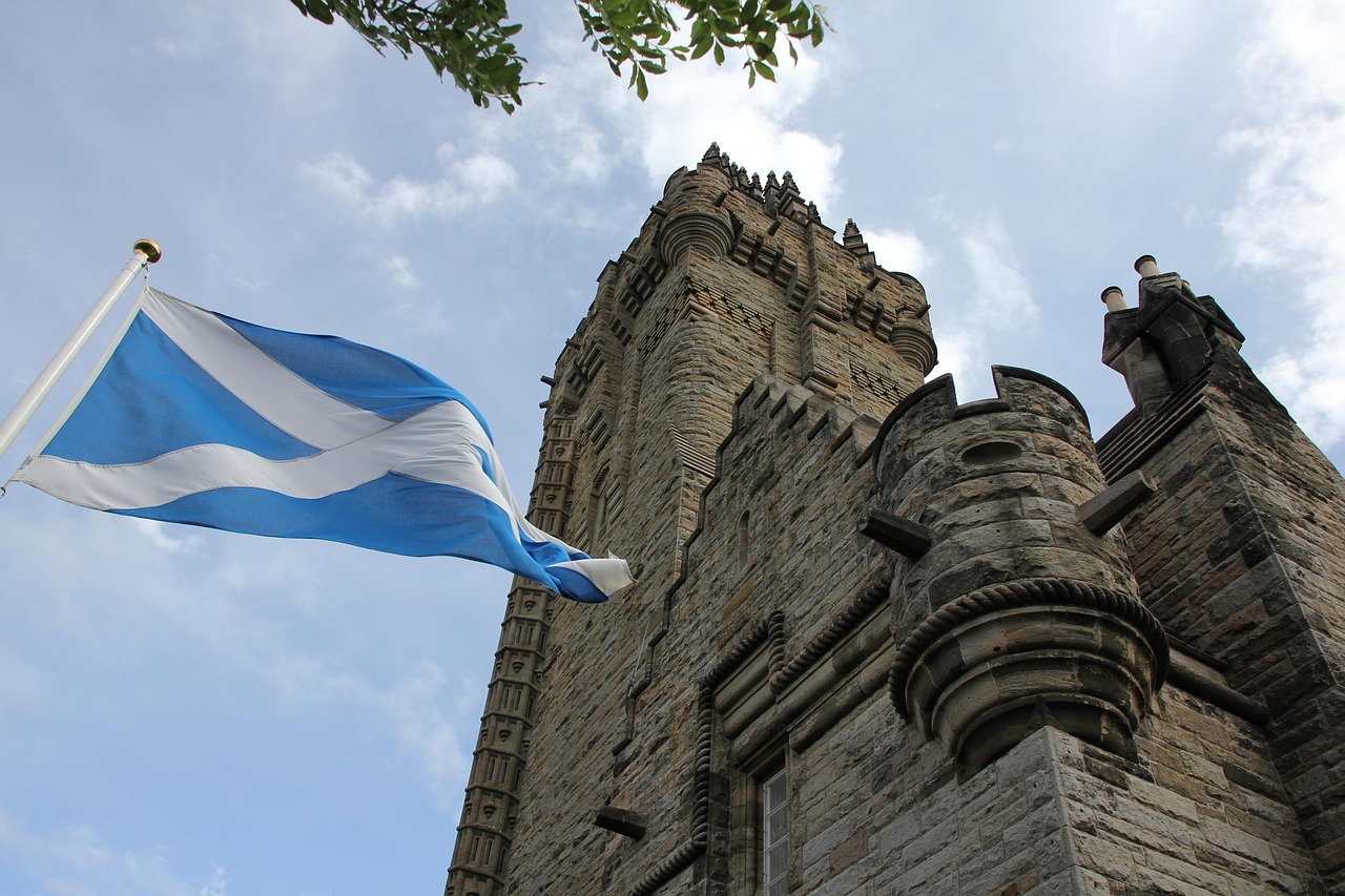 Torre William Wallace_ visita obligada en Stirling Scottish flag flying beside a stone tower under a cloudy sky.