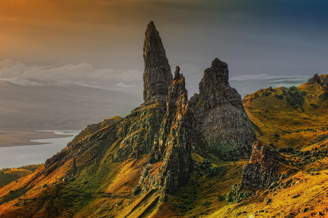 Rock formations on a grassy hill with a lake and cloudy sky in the background at sunrise.