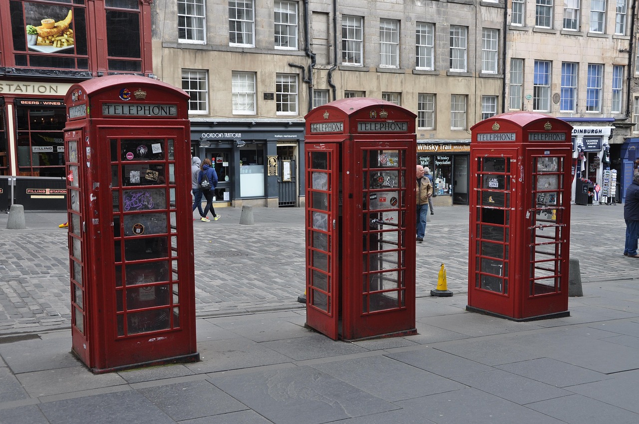 Three red British telephone booths on a cobblestone street.
