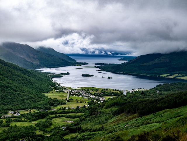 Cloudy day over a scenic lake surrounded by green hills and a small village.
