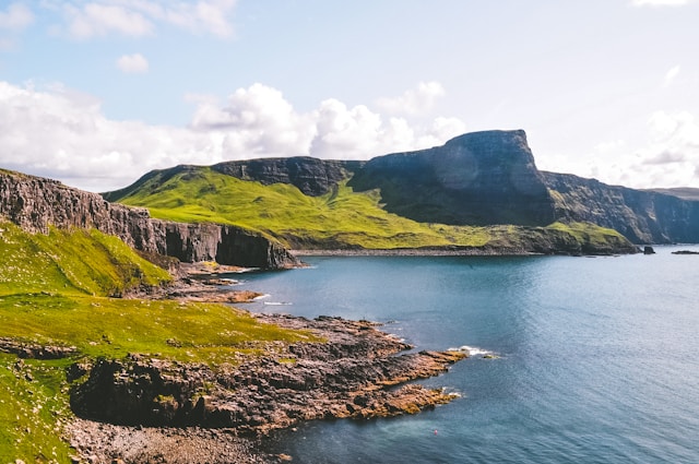 Coastal landscape with rugged cliffs and green hills under a clear sky.