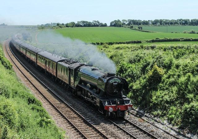 Steam train traveling through lush green countryside on a clear day.
