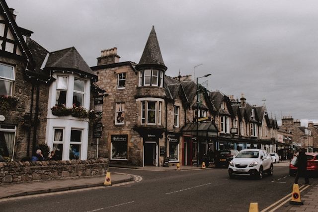 Street view with stone buildings, cars, and overcast sky.