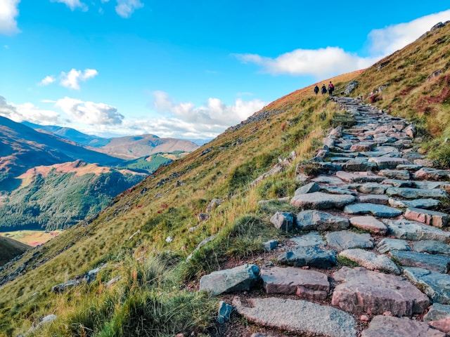 Stone path on a mountain slope under a blue sky with clouds.