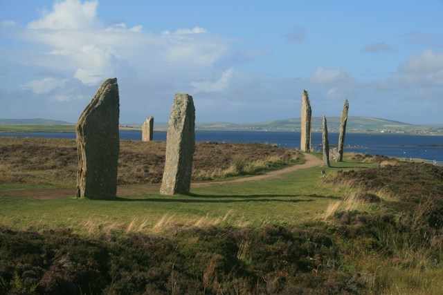 Stone circle on grassy field near water under clear sky.
