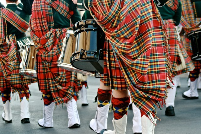 People in tartan kilts marching with drums at an event.